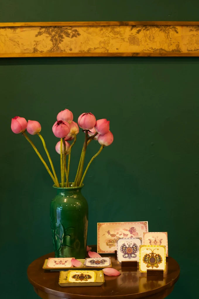 Pink lotus flowers beside illustrated souvenir pieces against an emerald wall